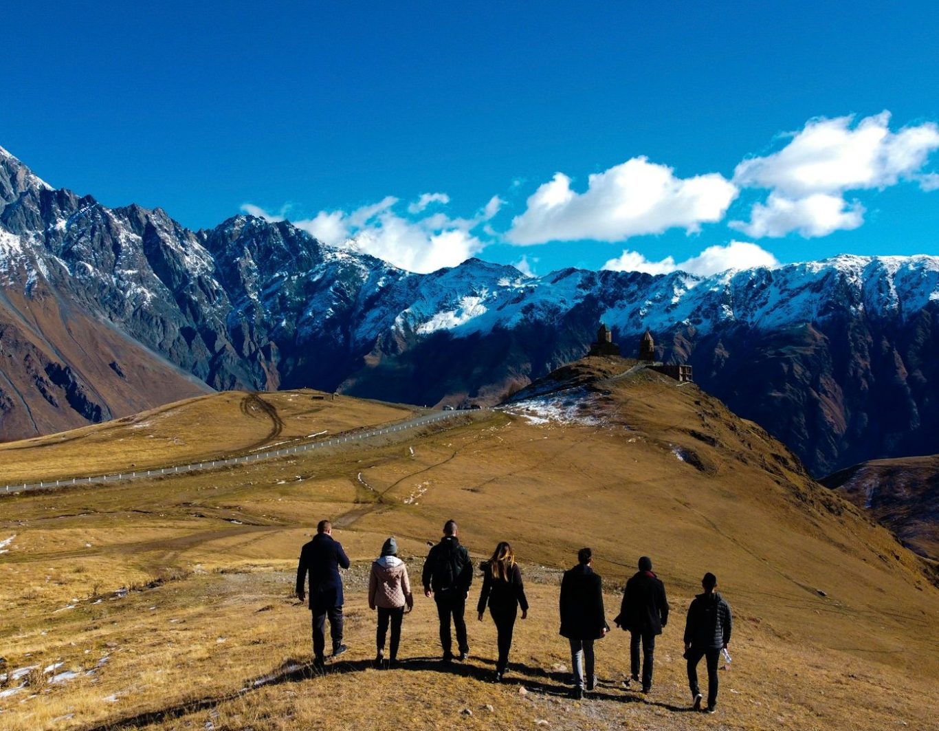 Séminaire immersif Groupe de six personnes marchant sur un sentier de montagne avec des sommets enneigés en arrière-plan.